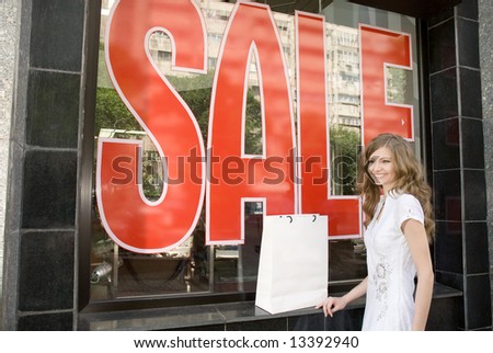 Woman with blank white shopping bag near shop window with sale sign