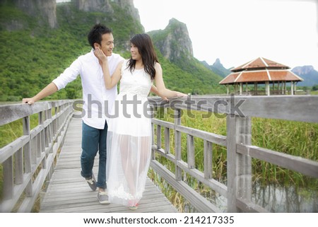The groom and the bride standing on the wooden bridge by the lake and looking at each other.
