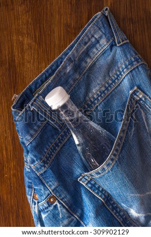 Bottled water in jeans pocket on wood background