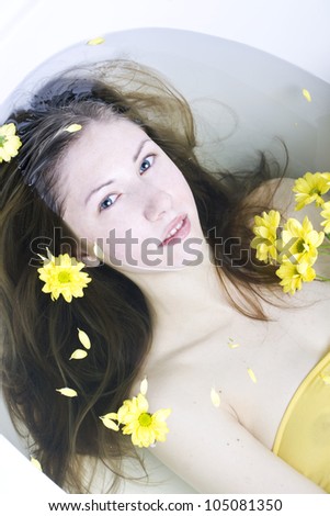 The young, beautiful woman with long hair in a bath with flowers