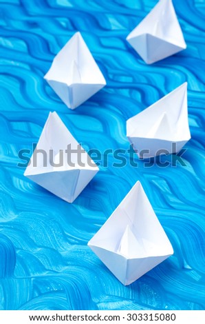 white paper origami boats on blue painted background