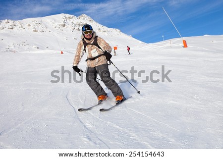 Winter ski resort in Alps. Alpine skier in ski mask skiing downhill.