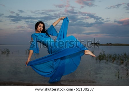 The beautiful girl in a dark blue dress poses in water in the form of a star