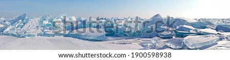 A panorama of the edge of a hummock field with beautiful huge blocks of transparent blue ice on the frozen Lake Baikal on a sunny frosty day. Cool natural background. Unusual winter landscape