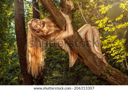 Wild guy with long hair weighs on the tree in the forest.