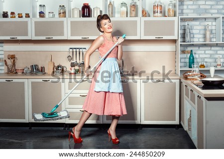 Happy girl makes cleaning the kitchen, hands holding a mop while singing.