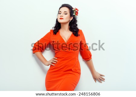 Girl in red dress posing in studio on a white wall.