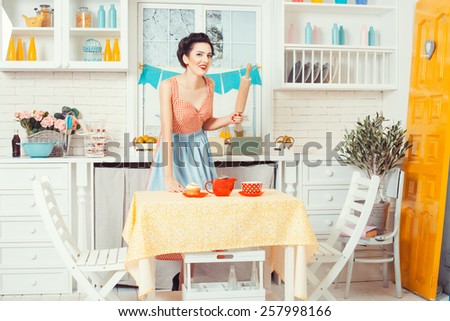 Pin-up girl style. Girl standing in the kitchen and smiles, in hands holds a rolling pin for the dough.