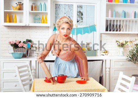 Woman in the kitchen in a retro style holding a rolling pin and pricked up her ears.