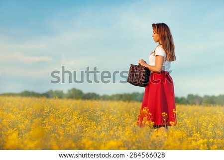 The girl in the profile. It stands on the field. Field of yellow flowers. In the hands holding a suitcase.