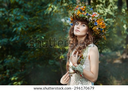 In the forest a cute girl. She has beautiful hair and a wreath of flowers on her head.