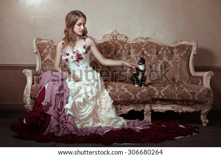 Girl in a beautiful dress with a train. She is sitting on an old couch.