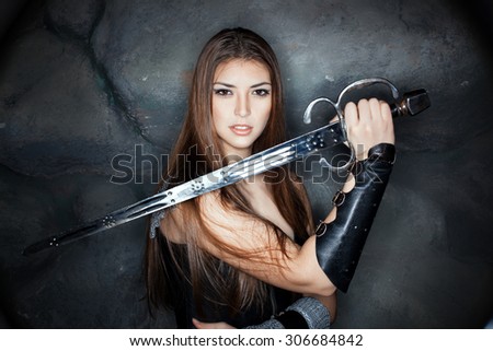 Beautiful girl holding a steel sword in his hand. Against the backdrop of a stone wall.