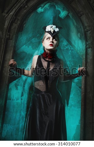 Scary girl standing in the doorway of an old castle. It causes fear, her eyes are white.
