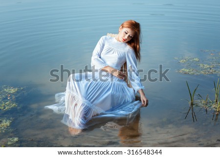 Girl in a white dress sitting on a chair in a lake. Her feet are in the water.