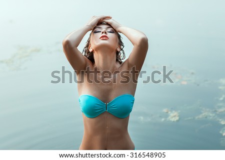Girl with wet body is in the lake water. It is in a bathing suit.