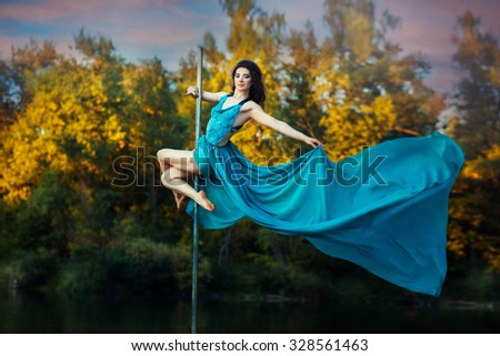 Girl high on a pole to dance her dress develops wind. She dances in nature.