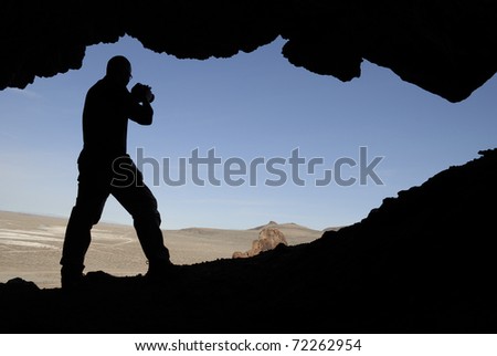 Silhouette of a man with a camera in an opening of a cave shooting out into the Nevada desert.