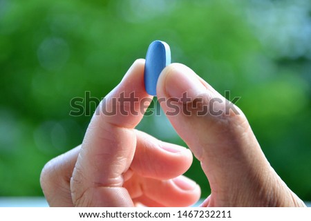 Hand of man holding blue pill. Closeup of a young man with a blue pill between  two fingers. Medicine pill. Medicine concept of viagra, medication for stomach, erection, sleeping, digestive, drugs  Stockfoto © 