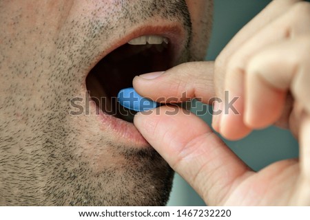 Hand of man holding blue pill. Closeup of a man taking blue medicine pill. Mouth view, illness. Medicine concept of viagra, medication for stomach, erection, sleeping, digestive or drugs Stockfoto © 
