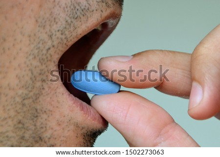 Hand of man holding blue pill. Closeup of a man taking blue medicine pill. Mouth view, illness. Medicine concept of viagra, medication for stomach, erection, sleeping, digestive or drugs Сток-фото © 