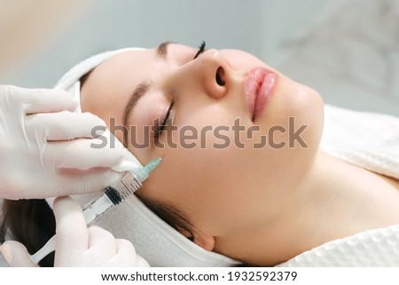 The doctor cosmetologist makes the rejuvenating facial injections procedure for tightening and smoothing wrinkles on the face skin of a beautiful, young woman in a beauty salon. Cosmetology, skincare Foto stock © 