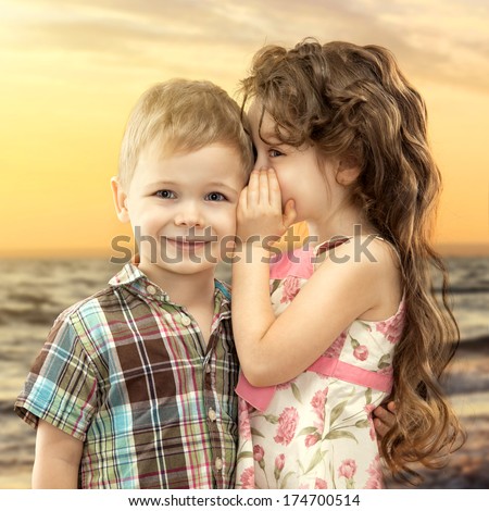 Little girl whispering something to boy on sea landscape at sunset. Love concept