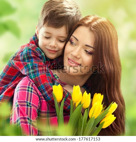 Son hugging happy mother with flowers. Mother`s day concept. Family holiday