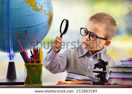 Boy looking through magnifying glass at globe, isolated on white background. School, education concept.