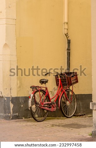A red bicycle with a basket leans against an old wall