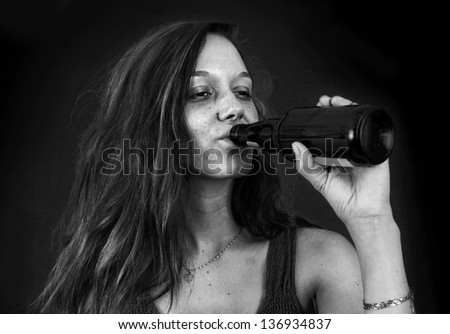 Dramatic black and white portrait of drunk young woman drinking beer over black