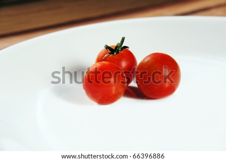 Three bright red ripe cherry tomatoes on a crisp white porcelain dinner plate placed on a wooden table.