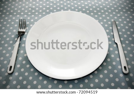 Empty white dinner plate with utensils on fun grey polka dot tablecloth.