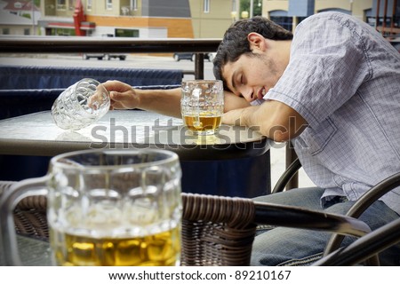 Young man passed out drunk with beer bocks on the glass table of an outdoor terrace: perfect for alcoholism, student hazing, beer binging and other related concepts.