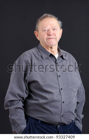 Portrait of an old or senior man smiling from the waist up with hands in his pockets shot in studio over black, great details.