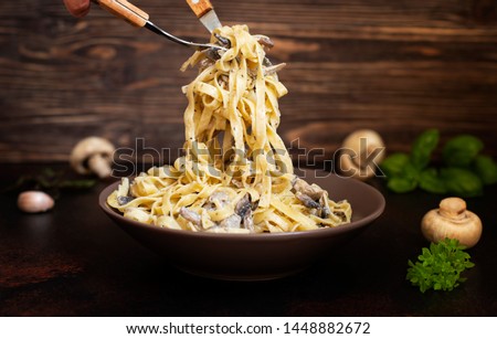 Homemade Italian fettuccine pasta with mushrooms and cream sauce (Fettuccine al Funghi Porcini). Traditional Italian cuisine. Served on a dark table with a rustic wooden background. Close-up