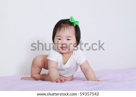 Very Pretty Nine Month Old Baby Asian Infant Girl Crawling on Pink Bed with Green Bow in Hair