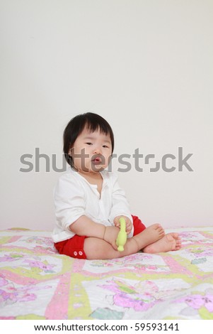 beautiful nine month old asian baby infant girl in white shirt and red pants with green teething toy