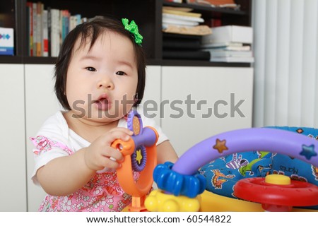 Beautiful ten month old asian infant baby girl in pink floral dress playing with toy