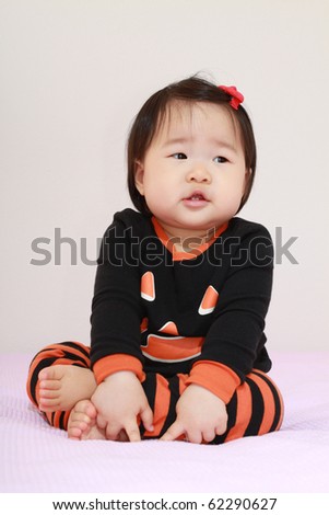 Beautiful ten month old baby asian infant girl in jack o lantern pajamas waiting anxiously for halloween