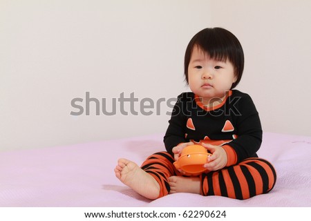 Beautiful ten month old baby asian infant girl in jack o lantern pajamas playing with halloween toy