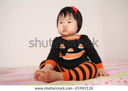 Beautiful Cute eleven month old baby asian infant girl in jack o lantern pajamas for halloween