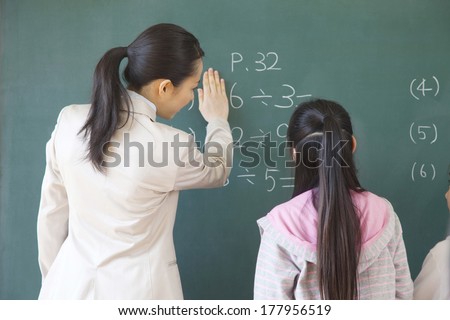 Female Japanese teacher standing next to the elementary Japanese girl who solves the problem of blackboard