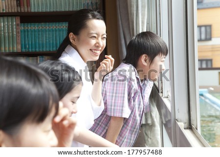 Female teacher and elementary students looking out from the window of the library
