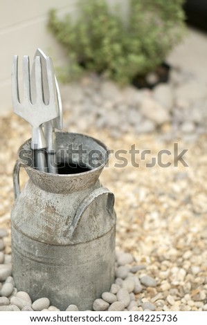 A gardening fork and trowel in an antique milk jug in the garden