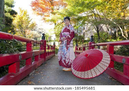 Middle-aged woman standing on a red ornamental bridge wearing Japanese traditional outfit