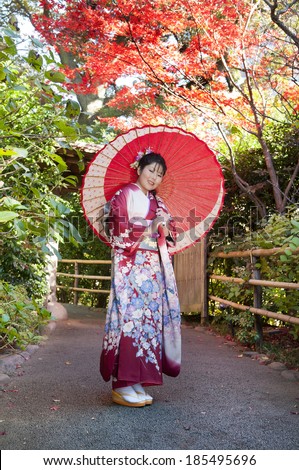 Asian woman holding decorative paper umbrella in garden while dressed in Japanese traditional outfit