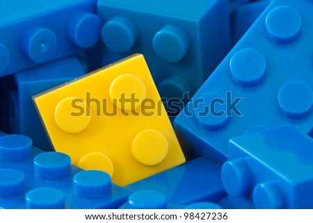 color toy background. yellow plastic brick in a middle of blue ones