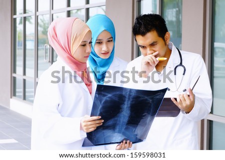 Experienced male doctor guide two female junior doctors examining a file in in front of hospital