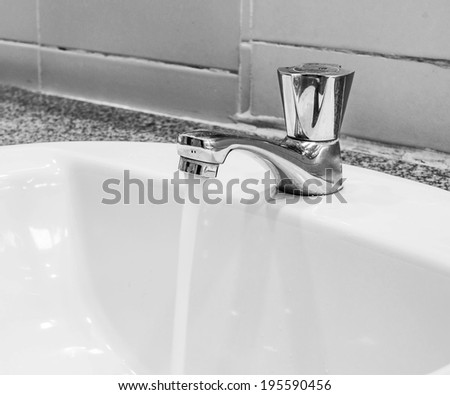 Open faucet, water is running, tinted black and white image